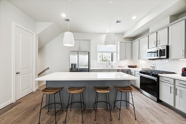 kitchen with tasteful backsplash, visible vents, a center island, appliances with stainless steel finishes, and a breakfast bar