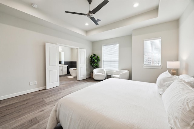 bedroom with connected bathroom, recessed lighting, wood finished floors, a raised ceiling, and baseboards