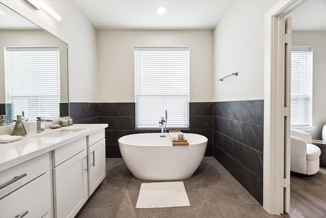 bathroom featuring tile walls, a freestanding bath, a wealth of natural light, and vanity