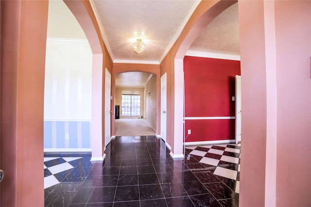hall featuring arched walkways, crown molding, a textured ceiling, and baseboards