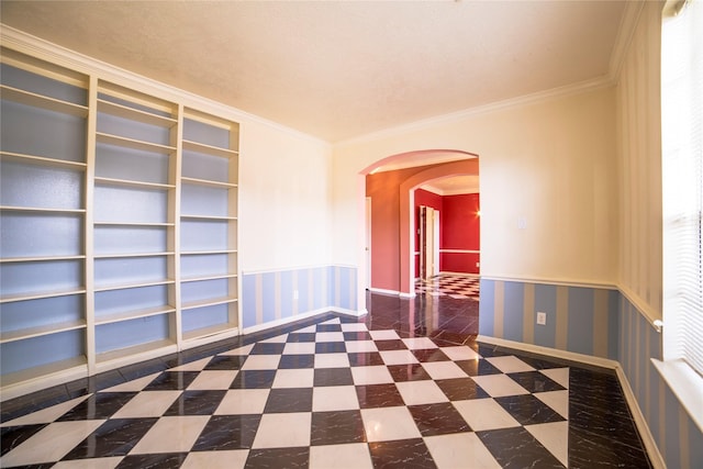 empty room with wainscoting, arched walkways, ornamental molding, and baseboards