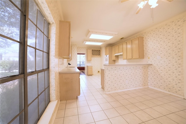 kitchen featuring a peninsula, light brown cabinetry, wallpapered walls, ceiling fan, and light tile patterned floors