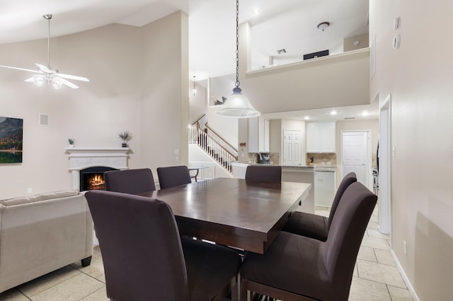 8322 Calico Canyon Dr, Tomball, TX 77375 - dining area with high vaulted ceiling, a ceiling fan, light tile patterned flooring, a warm lit fireplace, and stairs