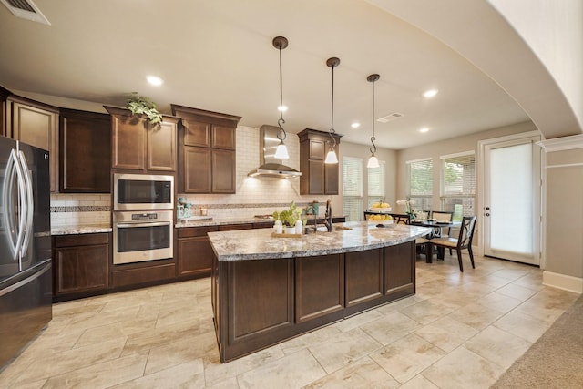 3225 Summer Tanager Ln, Manvel, TX 77578 - kitchen featuring stainless steel appliances, wall chimney exhaust hood, tasteful backsplash, arched walkways, and light stone countertops