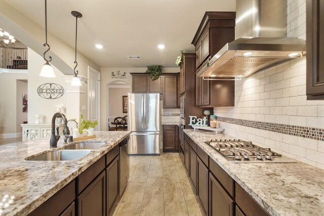 3225 Summer Tanager Ln, Manvel, TX 77578 - kitchen with wall chimney range hood, stainless steel appliances, a sink, backsplash, and light stone countertops