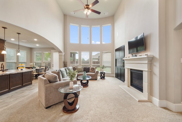 3225 Summer Tanager Ln, Manvel, TX 77578 - living room featuring ceiling fan, arched walkways, a glass covered fireplace, a towering ceiling, and light carpet