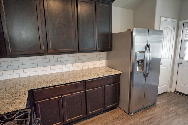 kitchen with dark wood-type flooring, dark brown cabinets, light stone counters, stainless steel fridge, and decorative backsplash