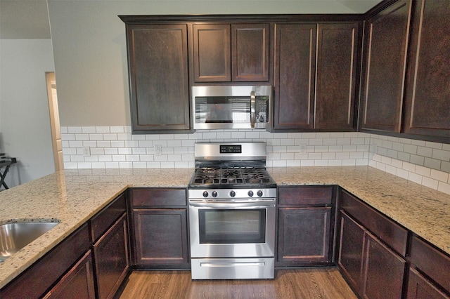 kitchen with light wood-type flooring, dark brown cabinetry, light stone countertops, and stainless steel appliances