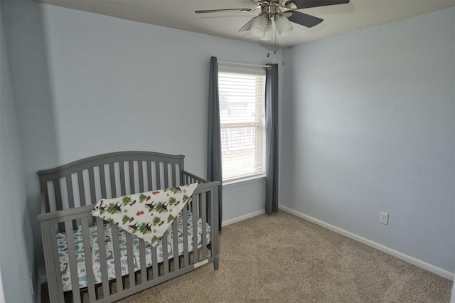 carpeted bedroom featuring a nursery area, baseboards, multiple windows, and ceiling fan