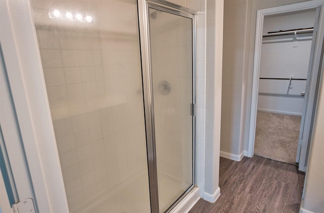 full bathroom featuring a spacious closet, baseboards, a stall shower, and wood finished floors