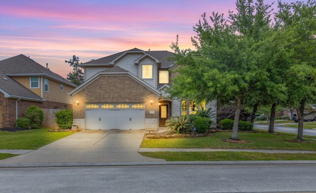 traditional-style house featuring a yard, brick siding, concrete driveway, an attached garage, and stone siding