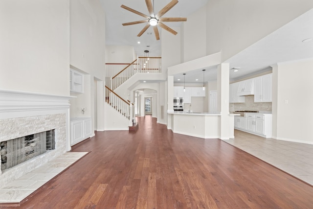 6214 Laguna Del Rey Dr, Houston, TX 77041 - unfurnished living room with a towering ceiling, a tiled fireplace, stairs, ceiling fan, and wood finished floors
