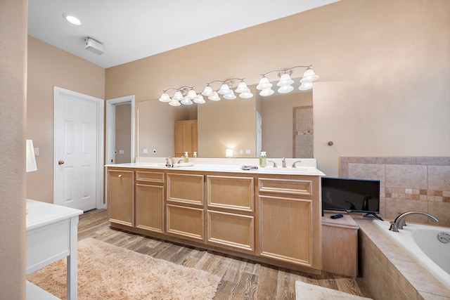 bathroom with a sink, double vanity, wood finished floors, and a garden tub