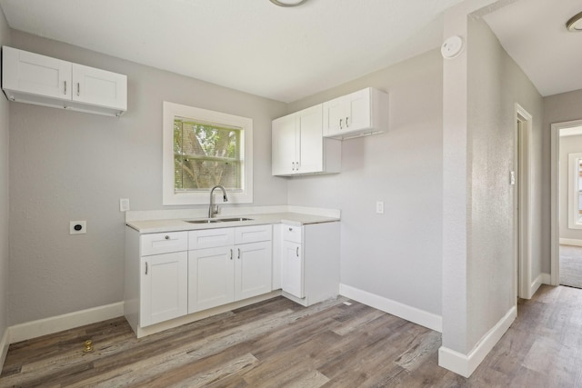 kitchen with white cabinets, baseboards, a sink, and light wood-style floors