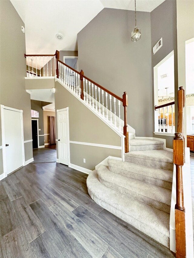 staircase with wood finished floors, visible vents, high vaulted ceiling, and baseboards