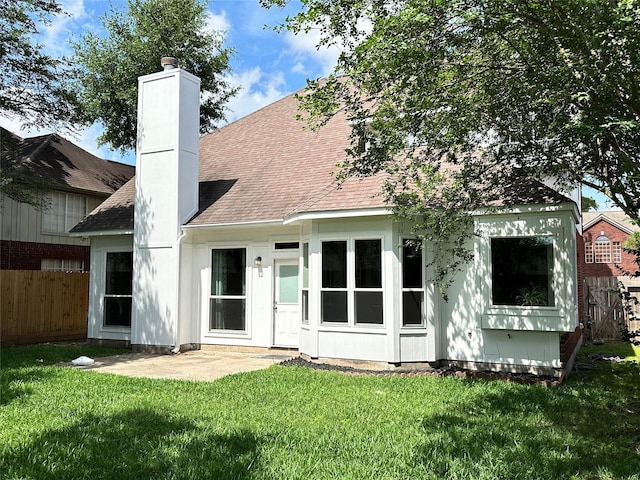 rear view of property with a yard, a chimney, a shingled roof, and fence