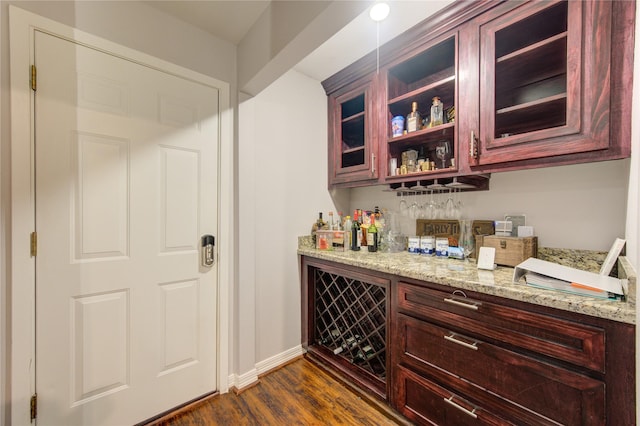 bar featuring a bar, dark wood-type flooring, and baseboards
