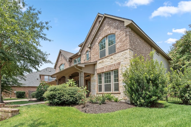 view of side of home with a yard, stone siding, fence, and brick siding
