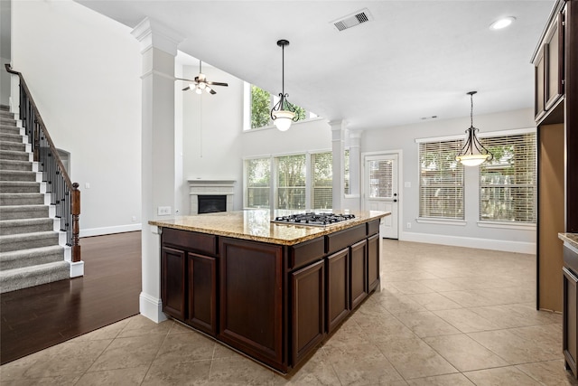 kitchen featuring baseboards, a fireplace, dark brown cabinets, ornate columns, and stainless steel gas stovetop