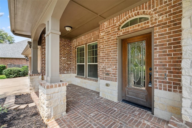 view of exterior entry featuring a porch and brick siding