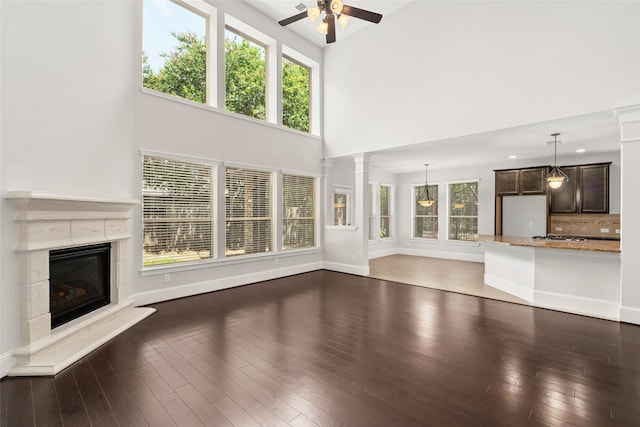 unfurnished living room featuring a glass covered fireplace, a towering ceiling, baseboards, ceiling fan, and wood finished floors