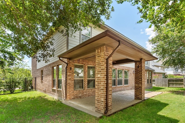 back of property with brick siding, fence, a patio, and a lawn