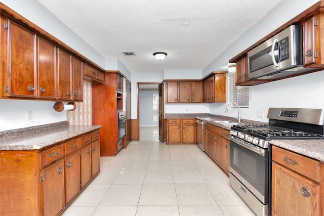 800 Fairway Dr, Richmond, TX 77469 - kitchen with brown cabinetry, a textured ceiling, visible vents, appliances with stainless steel finishes, and a sink