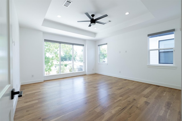 empty room featuring visible vents, wood finished floors, a raised ceiling, and ceiling fan