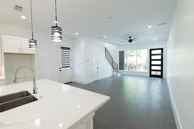 kitchen featuring a sink, visible vents, open floor plan, light stone countertops, and baseboards