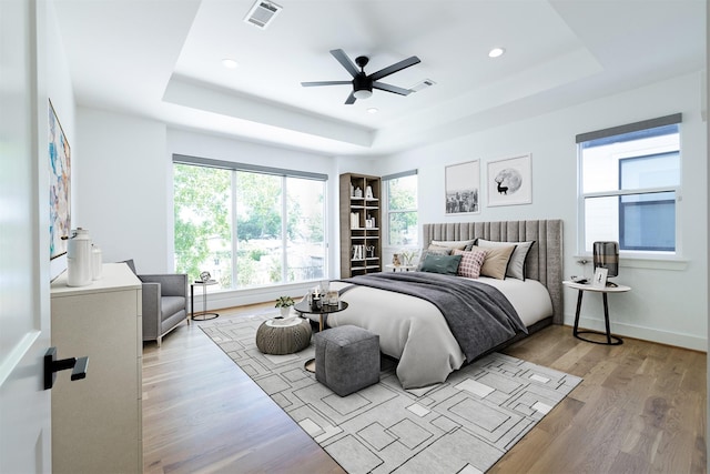 bedroom with light wood-type flooring, baseboards, a tray ceiling, and visible vents