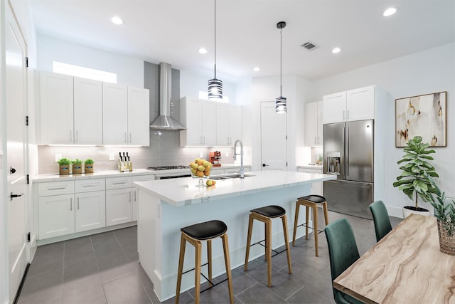 kitchen featuring wall chimney range hood, tasteful backsplash, a breakfast bar, visible vents, and stainless steel fridge with ice dispenser