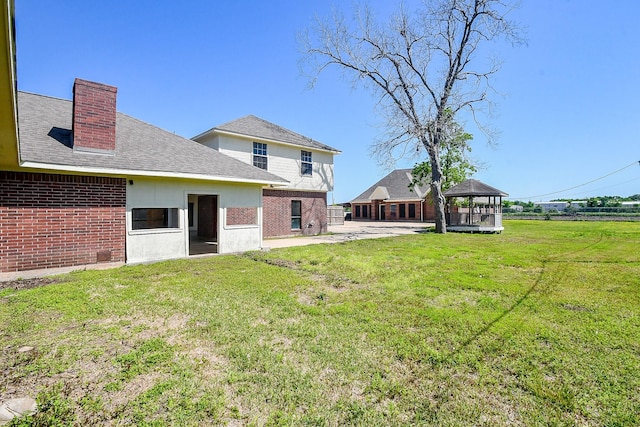 back of house with a gazebo, brick siding, a yard, and a chimney