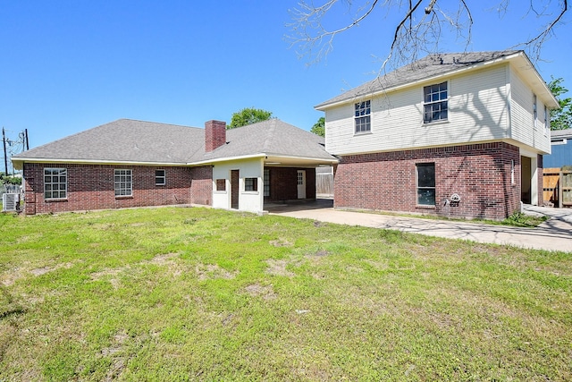 rear view of property with a yard, a carport, a patio area, a chimney, and brick siding