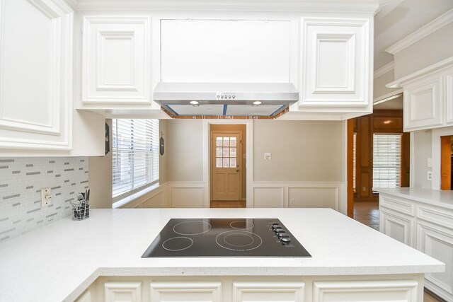 kitchen featuring tasteful backsplash, wall chimney exhaust hood, a decorative wall, light countertops, and black electric stovetop