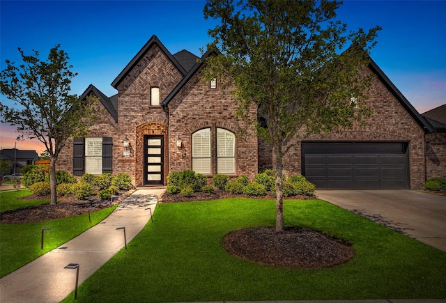 french country inspired facade featuring concrete driveway, a front lawn, brick siding, and a garage