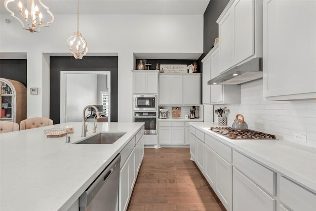 kitchen featuring under cabinet range hood, light countertops, a sink, a chandelier, and appliances with stainless steel finishes