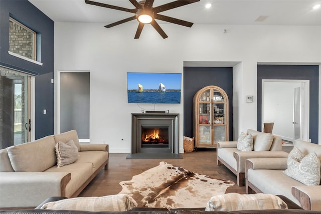 living area with a ceiling fan, wood finished floors, high vaulted ceiling, and a lit fireplace
