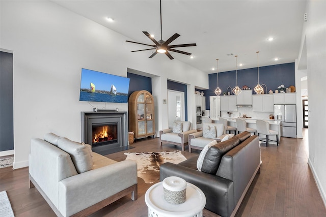 living area featuring a fireplace with flush hearth, dark wood-style floors, recessed lighting, a high ceiling, and ceiling fan
