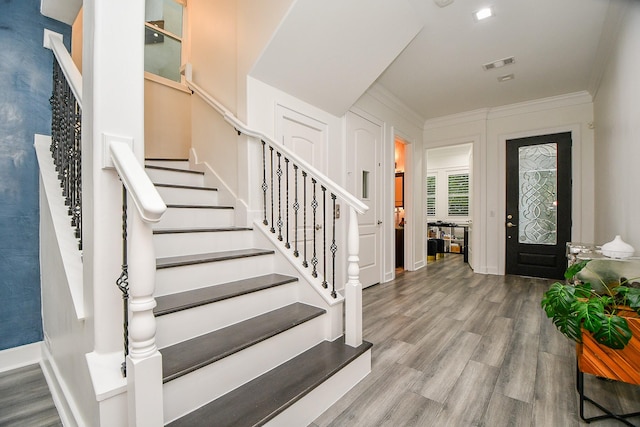 foyer entrance with ornamental molding, wood finished floors, visible vents, and stairway