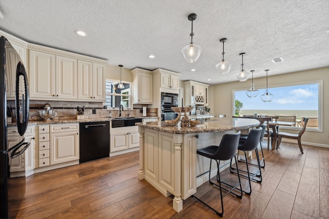 kitchen featuring plenty of natural light, cream cabinetry, black appliances, and wood-type flooring