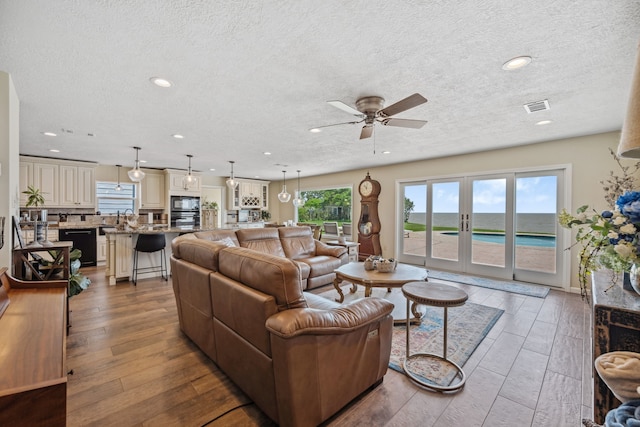 living room featuring a textured ceiling, plenty of natural light, visible vents, and a ceiling fan
