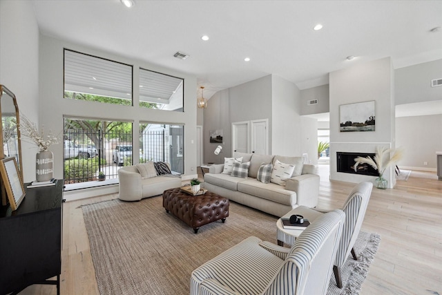 living area with a towering ceiling, recessed lighting, visible vents, and light wood-style floors