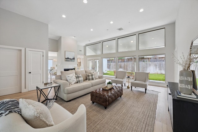 living area with a fireplace, a towering ceiling, recessed lighting, and light wood-style flooring