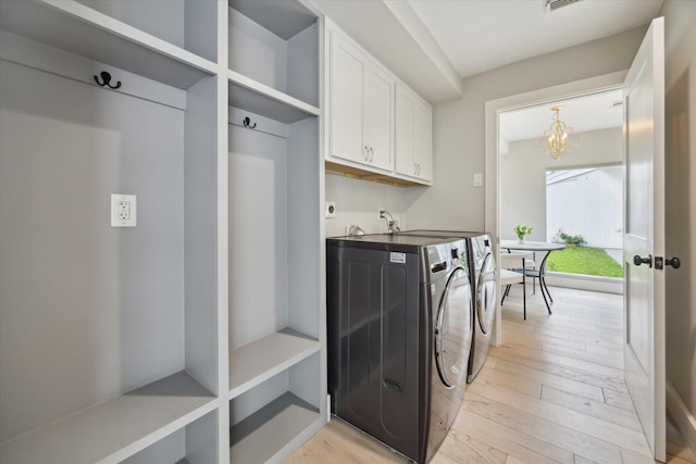 washroom featuring an inviting chandelier, light wood-type flooring, washer and clothes dryer, and cabinet space