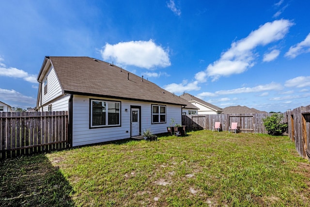 rear view of house featuring a lawn, a fenced backyard, and roof with shingles