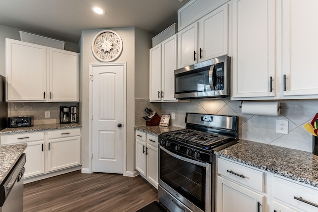 kitchen featuring dark wood-type flooring, dark stone counters, decorative backsplash, appliances with stainless steel finishes, and white cabinetry
