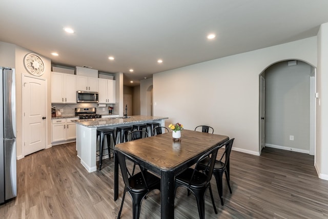 dining space with arched walkways, baseboards, and dark wood-style flooring