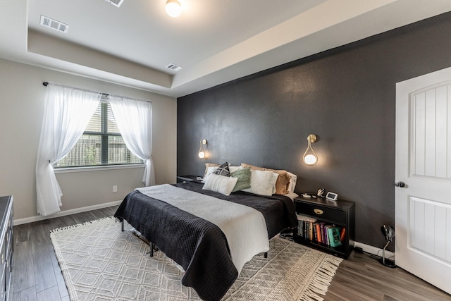 bedroom featuring a raised ceiling, wood finished floors, visible vents, and baseboards