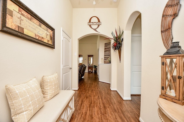 hall featuring a towering ceiling, baseboards, wood finished floors, and arched walkways