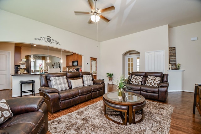 living area featuring arched walkways, a ceiling fan, dark wood-type flooring, and a towering ceiling